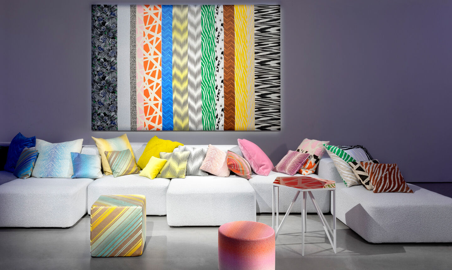 Multicoloured pillows and pouffs are placed near a white sofa from the 2023 Home collection
